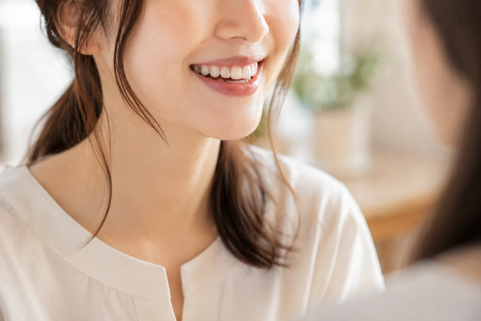 人と向かい合って笑う女性の斜めから見た口元のイメージ（イメージ写真・施術結果ではありません）